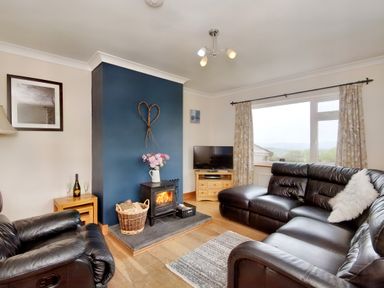 A living room with black leather sofas a wood burning stove and a television at Pen Y Gaer in Llannefydd near Abergele and Denbigh