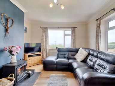 A living room with a black leather sectional sofa a wood burning stove and a television on a wooden stand at Pen Y Gaer in Llannefydd near Abergele and Denbigh