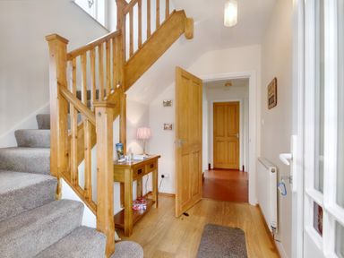 A hallway with wooden staircase and table with lamp next to open door leading to another room at Pen Y Gaer in Llannefydd near Abergele and Denbigh