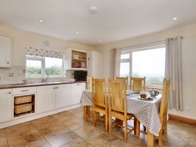A kitchen with a dining table and wooden chairs near windows at Pen Y Gaer Llannefydd near Abergele and Denbigh
