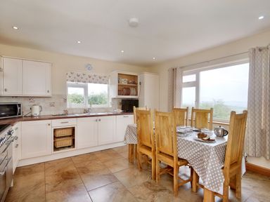 A kitchen with white cabinets a dining table with wooden chairs and a window with curtains at Pen Y Gaer in Llannefydd near Abergele and Denbigh