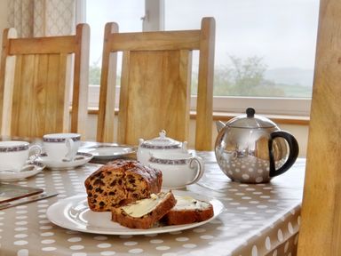 A dining table with a loaf of fruitcake and butter slices along with cups saucers a sugar bowl and a metal teapot at Pen Y Gaer in Llannefydd near Abergele and Denbigh
