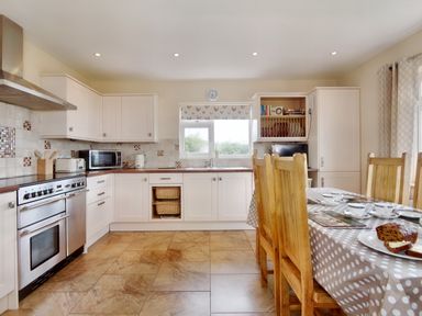 A kitchen with white cabinets wooden dining chairs and a table with a polka dot tablecloth at Pen Y Gaer in Llannefydd near Abergele and Denbigh