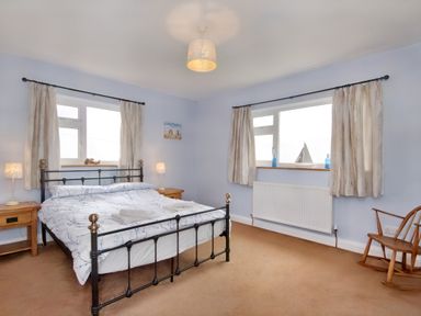 A bedroom with a double bed bedside tables lamps rocking chair and windows with curtains at Pen Y Gaer in Llannefydd near Abergele and Denbigh