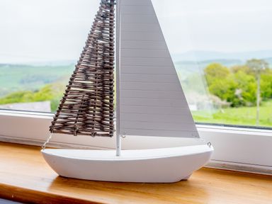 A decorative model sailboat on a wooden windowsill with a countryside view at Pen Y Gaer in Llannefydd near Abergele and Denbigh