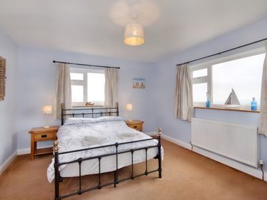 A bedroom with a double bed with white bedding two wooden bedside tables with lamps two windows with curtains and a radiator at Pen Y Gaer in Llannefydd near Abergele and Denbigh