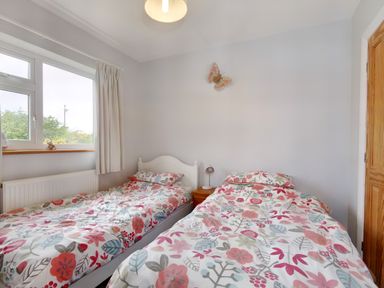 A bedroom with two single beds with floral bedding a small wooden nightstand with a lamp a window with curtains and a butterfly decoration on the wall at Pen Y Gaer in Llannefydd near Abergele and Denbigh