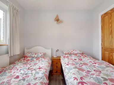 A bedroom with two single beds and floral duvet covers with a nightstand and lamp in between at Pen Y Gaer in Llannefydd near Abergele and Denbigh