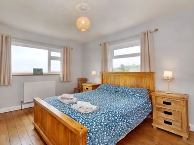 A bedroom with a wooden bed with blue patterned bedding and two folded towels on top with wooden bedside tables and lamps at Pen Y Gaer in Llannefydd near Abergele and Denbigh