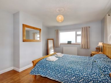 A bedroom with a wooden bed and blue patterned bedding two folded towels on the bed a wooden framed mirror on the wall a window with curtains and a standing mirror at Pen Y Gaer in Llannefydd near Abergele and Denbigh