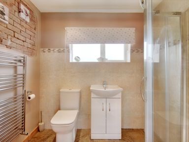A bathroom with a toilet and a sink under a window with a patterned blind at Pen Y Gaer in Llannefydd near Abergele and Denbigh