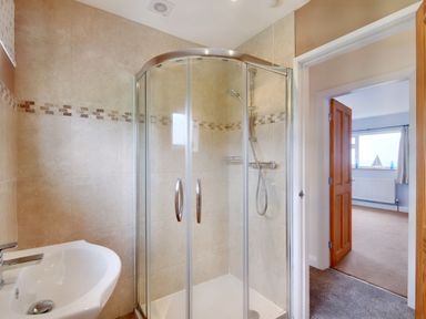A bathroom with a corner shower enclosure and sink next to an open door showing a room with a window at Pen Y Gaer in Llannefydd near Abergele and Denbigh