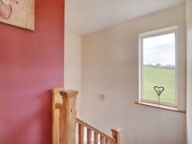 A stairway with wooden banisters next to a window and a red wall at Pen Y Gaer in Llannefydd near Abergele and Denbigh