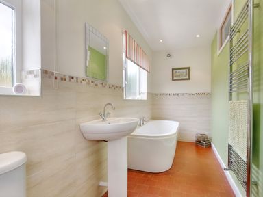 A bathroom with a white bathtub pedestal sink toilet towel rack and two windows at Pen Y Gaer in Llannefydd near Abergele and Denbigh