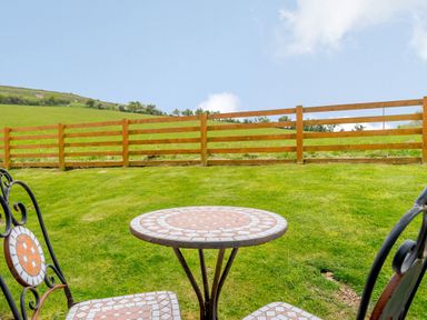 A patio set with two chairs and a round tiled table on grass near a wooden fence at Pen Y Gaer in Llannefydd near Abergele and Denbigh