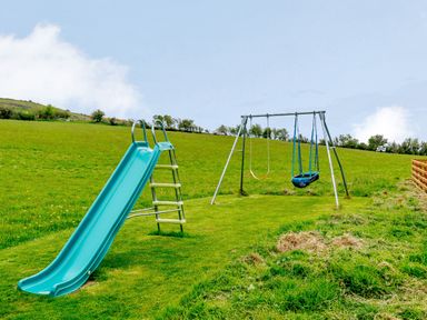 A blue slide and a swing set with two swings in a grassy outdoor area at Pen Y Gaer in Llannefydd near Abergele and Denbigh