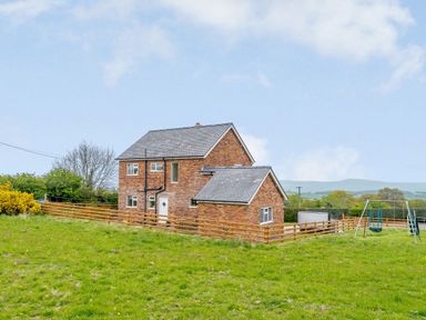 A brick house with a fenced yard and a swing set on grassy land at Pen Y Gaer in Llannefydd near Abergele and Denbigh