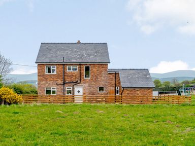 A brick house with a grey tiled roof and several windows surrounded by a wooden fence and green grass at Pen Y Gaer in Llannefydd near Abergele and Denbigh