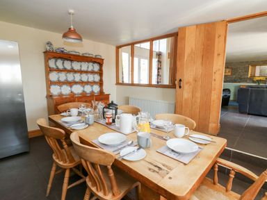 A dining room with a wooden table set for breakfast and a plate rack with blue and white plates at Mill Cottage in Aberaeron