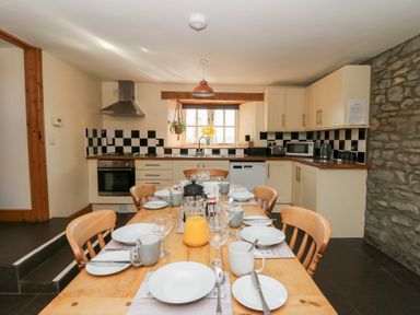 A kitchen with a wooden dining table set for breakfast and checkered tiled backsplash at Mill Cottage in Aberaeron