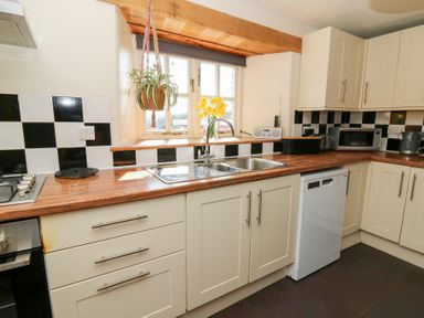 A kitchen with white cabinets wooden countertops a double sink a dishwasher and a checkered black and white tile backsplash at Mill Cottage in Aberaeron