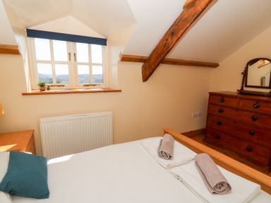 A bedroom with a bed, rolled towels, wooden dresser with mirror, and a window with a view at Mill Cottage in Aberaeron