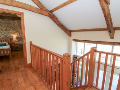 A wooden staircase with railing and ceiling beams next to a bedroom with stone wall at Mill Cottage in Aberaeron