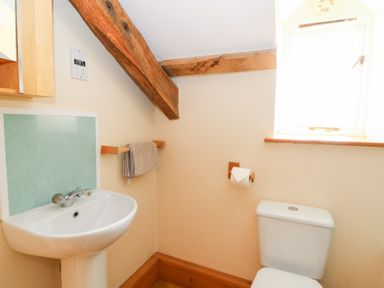 A bathroom with a white sink, a toilet, a towel rack with a towel, and a window with wooden beams at Mill Cottage in Aberaeron