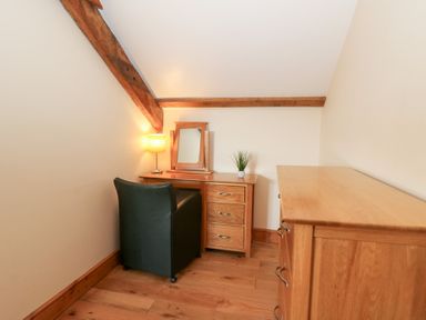 A small room with a wooden desk with drawers a mirror a lamp and a plant a black chair and a wooden chest of drawers at Mill Cottage in Aberaeron