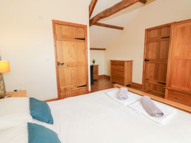 A bedroom with a bed with blue pillows and rolled towels on top wooden furniture and exposed ceiling beams at Mill Cottage in Aberaeron