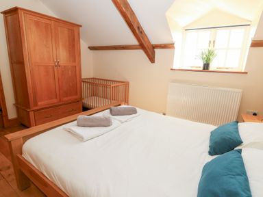 A bedroom with a wooden bed, wardrobe, crib, and a window with a plant at Mill Cottage in Aberaeron