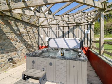 An outdoor hot tub with a pergola above and a stone wall on one side at Mill Cottage in Aberaeron