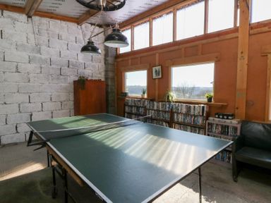 A room with a ping pong table shelves with DVDs a black chair and windows with views at Mill Cottage in Aberaeron