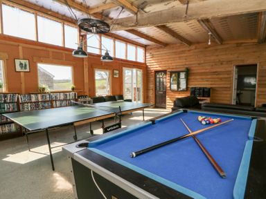 A game room with a pool table and ping pong table next to windows and a door at Mill Cottage in Aberaeron