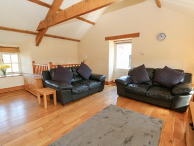 A living room with two black leather sofas with dark cushions wooden floor and exposed wooden ceiling beams at The Stable in Aberaeron