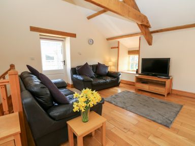 A living room with leather sofas a television a wooden table with flowers and wooden beams at The Stable in Aberaeron