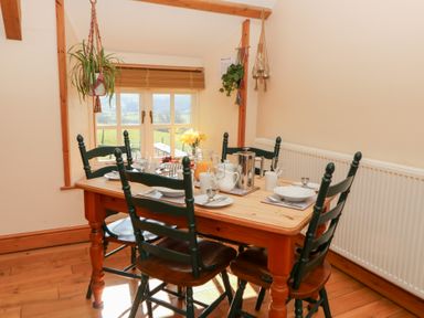 A dining area with a wooden table set with plates cups and glasses and four chairs near a window at The Stable in Aberaeron