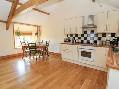A kitchen with wooden floors dining table with chairs and white cabinets at The Stable in Aberaeron