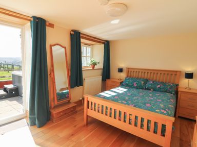 A bedroom with a wooden bed with floral bedding beside wooden nightstands and a mirror at The Stable in Aberaeron