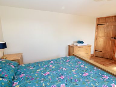 A bedroom with a floral bedspread a wooden chest of drawers and a bedside table with a lamp and a wooden door at The Stable in Aberaeron