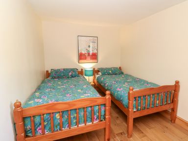 A bedroom with two wooden single beds with floral bedding a nightstand with a lamp and a framed picture on the wall at The Stable in Aberaeron