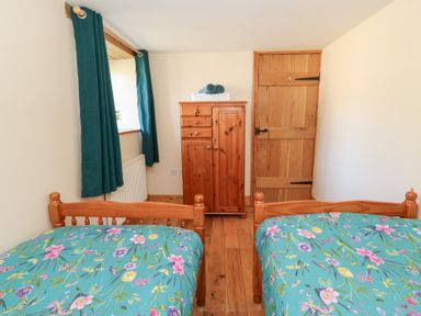 A bedroom with two single wooden beds with floral bedding a wooden dresser and a wooden door with teal curtains at The Stable in Aberaeron