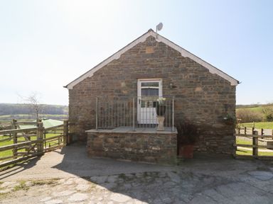 Stone building with a small raised porch and metal railing with a door and flower pot at The Stable in Aberaeron