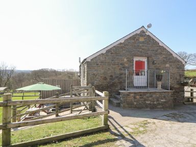 A stone building with a small porch and red door next to a fenced outdoor area with a green umbrella at The Stable in Aberaeron