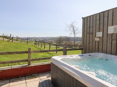 An outdoor hot tub next to a wooden fence with a grassy field and hills in the background at The Stable in Aberaeron