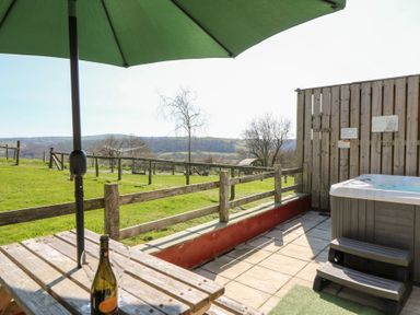 An outdoor patio with a wooden table and umbrella bottle and glasses on the table fenced grass field and hills in the background at The Stable in Aberaeron