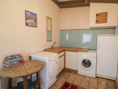 A utility room with a washing machine dryer wooden table with books fridge and a mirror at The Stable in Aberaeron