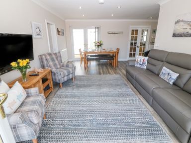 A living room with gray sofa and armchairs a wooden dining table with chairs and flowers on the table at St Winifreds in Rhosneigr