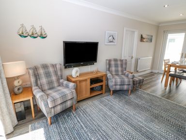 A living room with two plaid armchairs a wall-mounted television and a wooden side table at St Winifreds in Rhosneigr