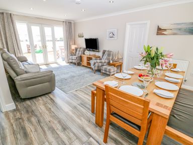 A living room with a sofa chairs a wooden dining table set with plates glasses and flowers at St Winifreds in Rhosneigr